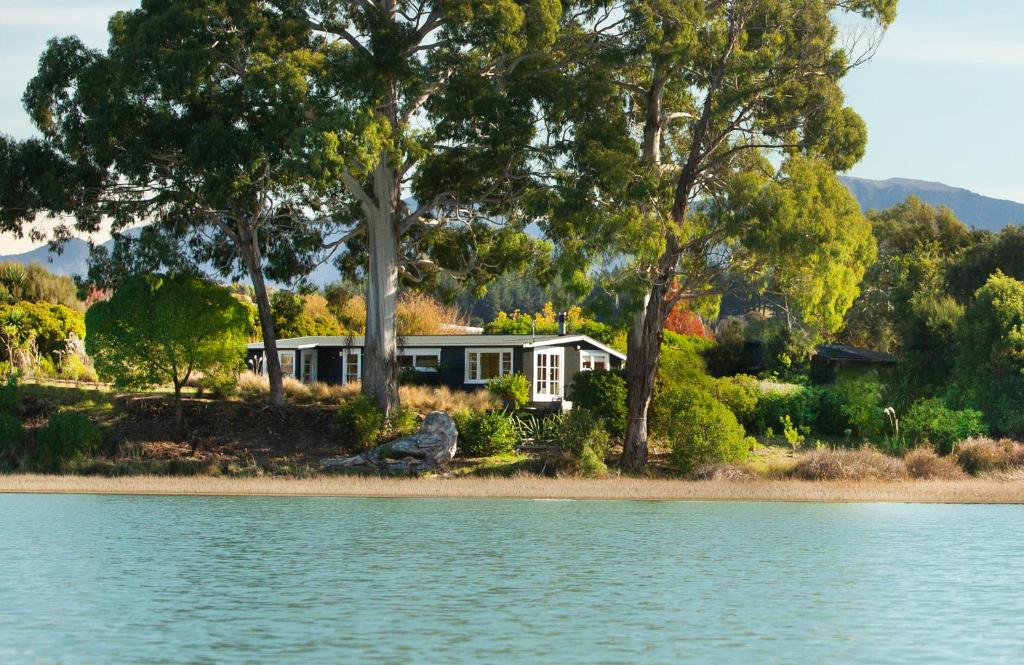 Single cottage surrounded by tall trees beside calm water at Apple Pickers Cottages in Mapua, Tasman District Apple Pickers Cottages - Mapua - Tasman District New Zealand